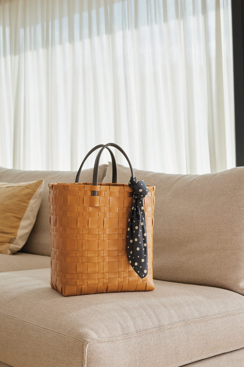 Die gelbe handgeflochtene BLISS Handtasche steht auf einem weißen Sofa in einem Wohnzimmer